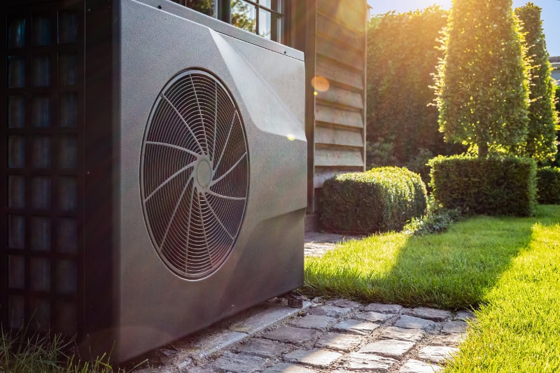 A heat pump next to a home and some green grass.
