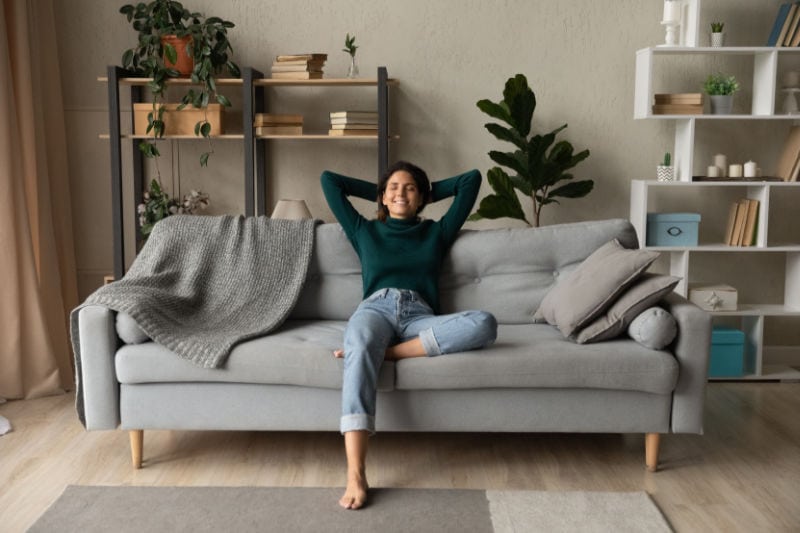 A woman relaxing on a gray couch in her living room.