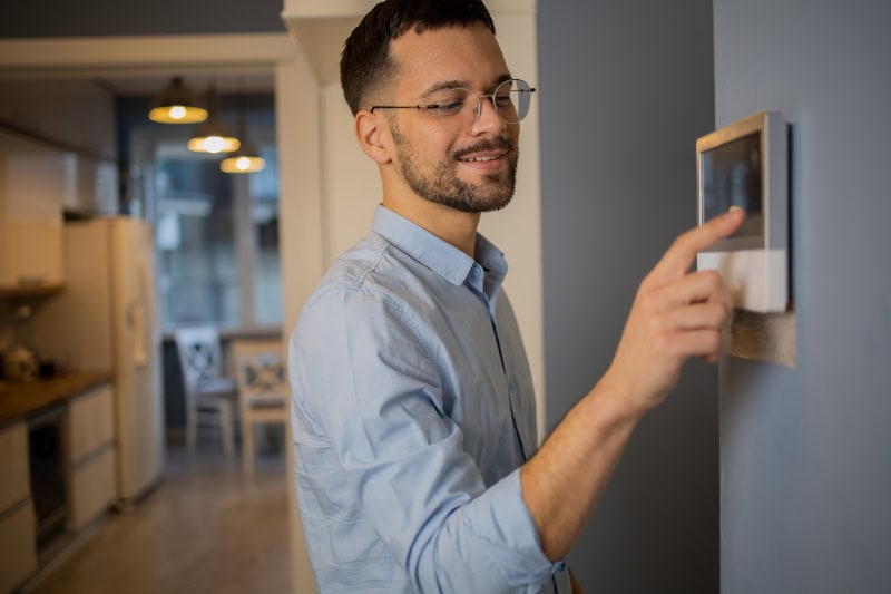 A man adjusting the temperature on the thermostat in his home.